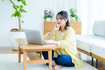 自宅でノートパソコンを操作しながら考える若い女性