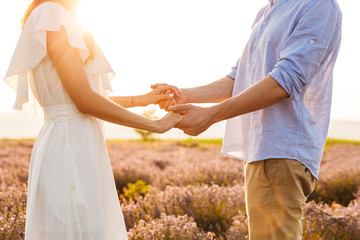 Cropped image of young couple man and woman holding hands, while walking outdoor in lavender field during dating