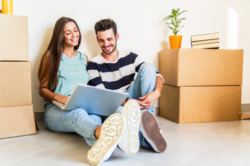 Happy couple sitting of the floor moving in the new house using the computer