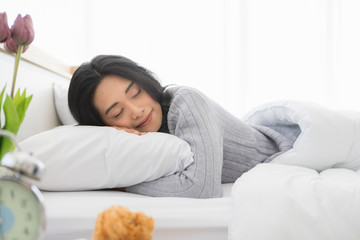 Asian woman lies on one's side on bed in bedroom..
