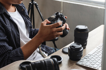 Young man photographer sitting and press button of professional camera to review shoot or setting camera at home office studio. 