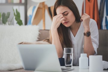 Asian beautiful women stressful and headache after working with a laptop for a long time.Hand holding the face After taking a headache medication.Office syndrome concept.