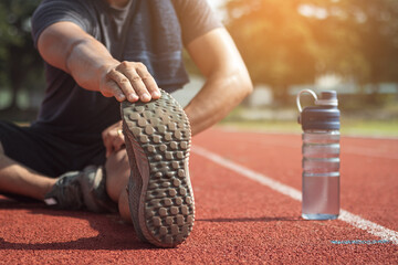 Runner man is stretching legs preparing for run training on track.