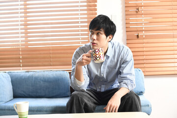 室内で飲み物を飲むリラックス中の若いアジア人男性