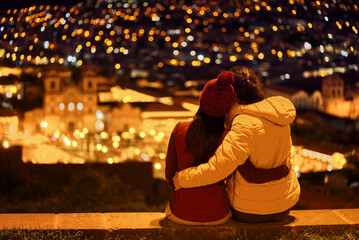 Pareja de turistas sentados en el mirador mirando la plaza de Cuzco iluminada